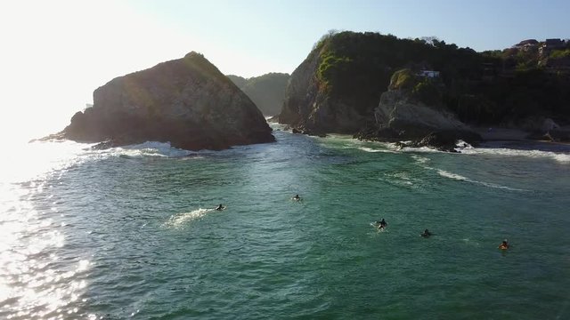 Surfers waiting for waves beside dramatic rock cliffs as the drone flies overhead and in between the cliffs.