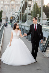 Bride and groom hugging in the old town street. Wedding couple walking on Szechenyi Chain Bridge, Hungary. Happy romantic young couple celebrating their marriage. Wedding and love concept.