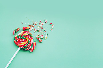 Broken in pieces candy on a stick. Smashed lollipop on green background, top view with copy space.