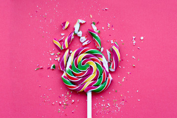 Broken in pieces candy on a stick. Smashed lollipop on pink background, top view.