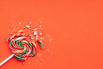 Broken in pieces candy on a stick. Smashed lollipop on orange background, top view with copy space.