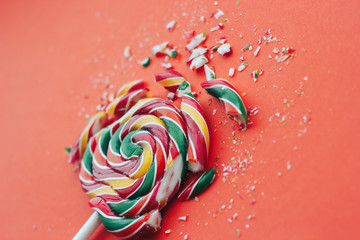 Broken in pieces candy on a stick. Smashed lollipop on orange background.