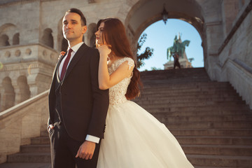 Bride and groom hugging in the old town street. Wedding couple walking on the Fisherman's Bastion, Budapest, Hungary. Happy romantic young couple celebrating their marriage. Wedding and love concept.