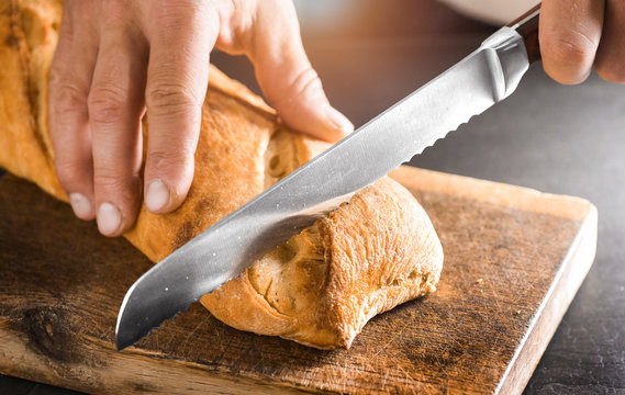 Man cutting fresh bread with knife on wood board. Healthy eating and traditional bakery concept