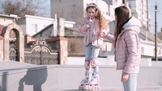 A Pretty Mother Is Spending Time With Her Cute Daughter. The Family Is Going Out For A Walk. The Kid Is Going Roller-skating. The Woman Is Helping The Child Skate.