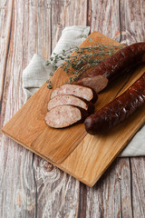 Industrial manufacture of sausages. Smoked sausage on a wooden rustic table with addition of fresh aromatic herbs and spices, natural product from organic farm, produced by traditional methods.