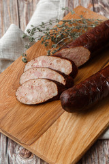 Industrial manufacture of sausages. Smoked sausage on a wooden rustic table with addition of fresh aromatic herbs and spices, natural product from organic farm, produced by traditional methods.