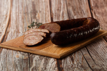 Industrial manufacture of sausages. Smoked sausage on a wooden rustic table with addition of fresh aromatic herbs and spices, natural product from organic farm, produced by traditional methods.