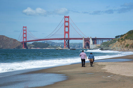 Couple walking on the beach with San Fransico's iconic Golden Gate Bridge in the background