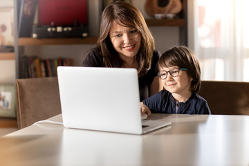Mother and boy studying with laptop in home.