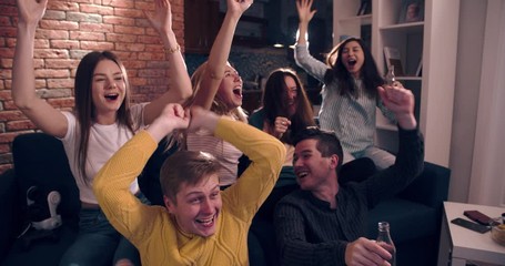 Very excited friends having fun by watching football match, drinking beer and soda and eating popcorn and chips at home. Friends watching football at home and yelling goal with raised hands
