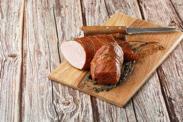 Smoked ham on a chopping board. Sliced smoked gammon on a wooden table with addition of fresh herbs and aromatic spices. Natural product from organic farm, produced by traditional methods