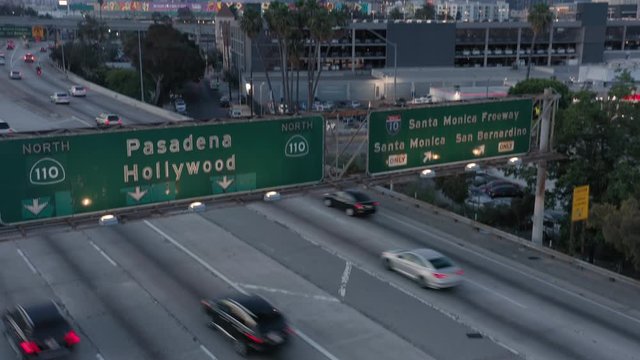 Los Angeles. Downtown. 2019. Aerial view of the green road information sign above the highway 110. Sunset time. The freeway is busy with traffic. A group of skyscrapers is seen ahead. 4K