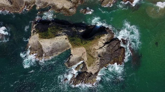 Drone looking straight down on a tropical coastal rock outcrop at midday with surging surf.