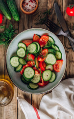 Healthy vegetable salad of fresh tomato, cucumber, dill and spices and oil in bowl on rustic wooden background. Diet concept.
