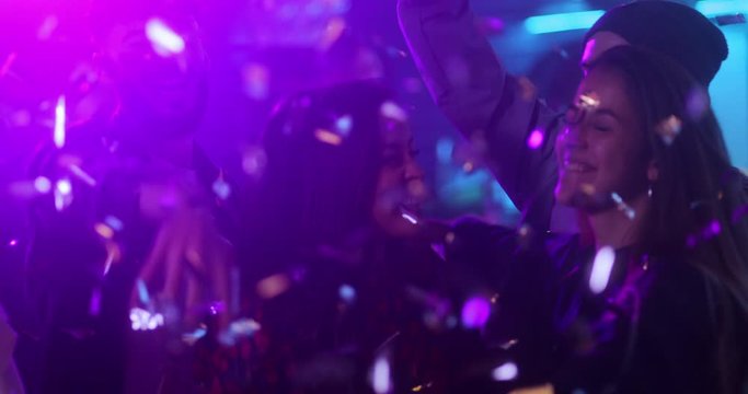 Multi-ethnic group of friends dancing together, throwing confetti inside bar