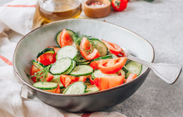 Healthy vegetable salad of fresh tomato, cucumber, dill and spices and oil in bowl on light gray background. Diet concept.