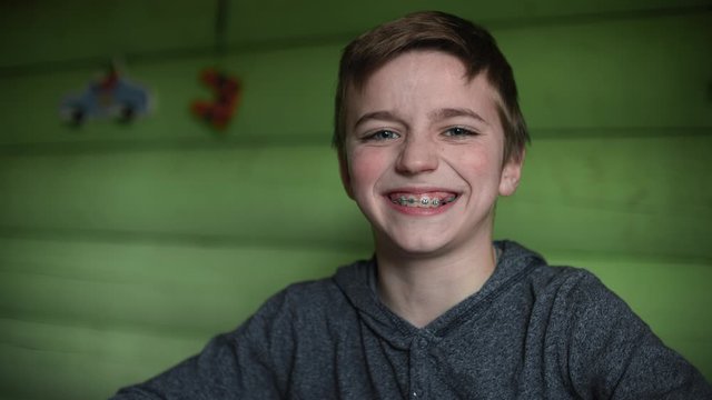 Smiling teenage boy with braces looking at camera. Close-up portrait with green background.