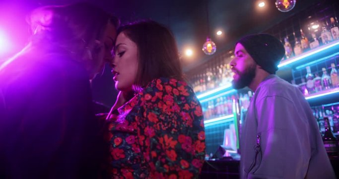 Attractive young lesbian couple and friends dancing inside trendy bar