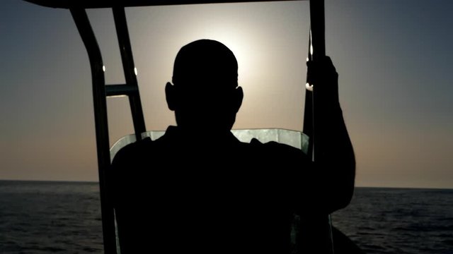 Rear shot behind a silhouette speed motorboat helmsman skipper navigating fast in sea with sun in background