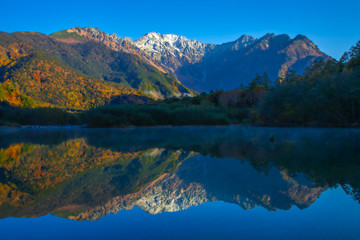 紅葉の上高地大正池から初冠雪した穂高連邦と水面に鮮やかに映り込み水鏡の風景写真