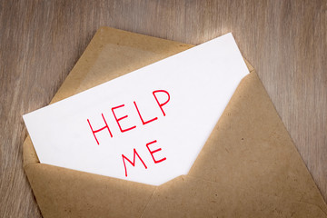 The phrase help me, written in red by hand on a white sheet of paper, lies in a craft envelope