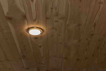 Luminous white spotlight on a ceiling covered with a wooden panel (larch)
