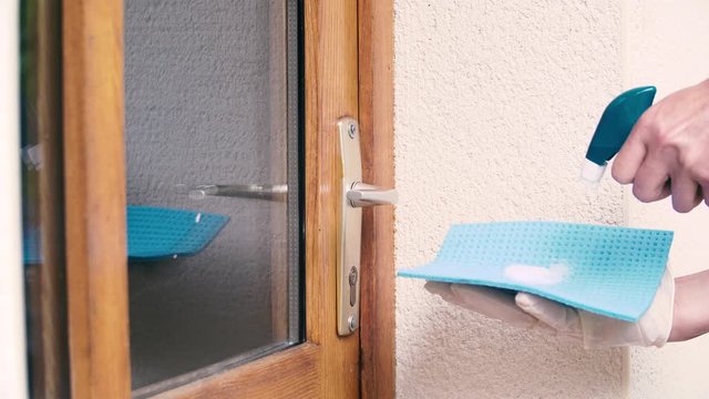 Nettoyage par d&eacute;sinfection en pulv&eacute;risant un antisepsie  assainissent sur une poign&eacute;e de porte m&eacute;tallique, muni de gant a usage unique.