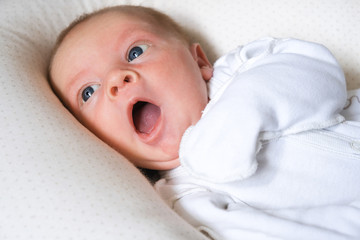 Yawning cute newborn baby boy lying in bed trying to sleep. Baby sleeplessness.