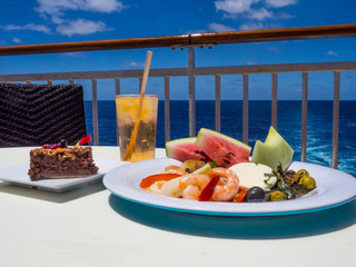 Plate of colorful fruit and shrimp from cruise ship buffet sits on outside table with sea and...
