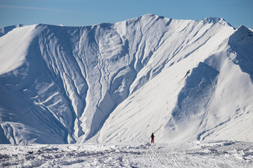 Small man on the background of a huge massive snowy mountain in winter at a ski resort