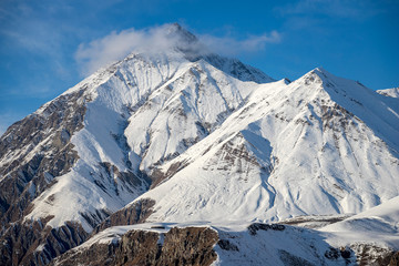 Fototapeta na wymiar Beautiful sharp mountain peak in the snow and a small cloud on it