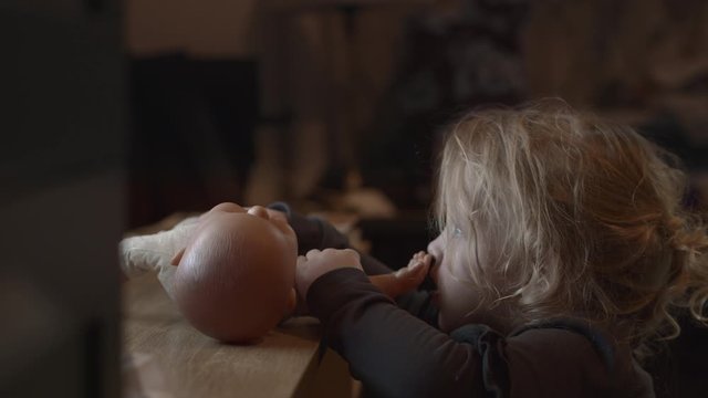 Slow motion shot of toddler girl watching TV and pulling the hand of the doll into the mouth
