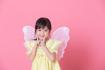 Little sweet girl dressed up with angel wings and toothy smile in pink background.