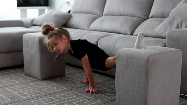 Little cute girl is practicing gymnastics at home. Online training. Stretching, twine