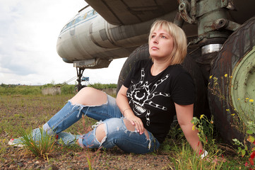Blonde model sitting near a old plane