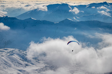 Paraglider flies in the clouds over the mountains
