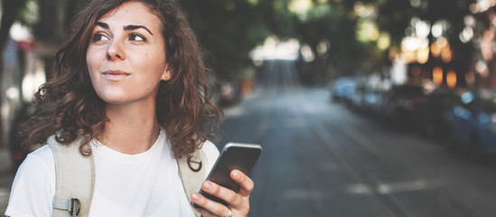 Handsome curly brunette woman with mobile phone walking on the street. Wide screen, panoramic