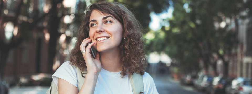 Curly Woman Talking On The Mobile Phone. Walking Along The Street With Backpack And Traveling. Wide Screen, Panoramic