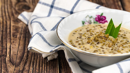 "Bubur kacang hijau" or mung beans porridge is a Malaysian traditional dish usually eat as starter or desert. Made from mung beans, coconut milk & palm sugar. Isolated over wooden background.