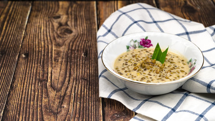 "Bubur kacang hijau" or mung beans porridge is a Malaysian traditional dish usually eat as starter or desert. Made from mung beans, coconut milk & palm sugar. Isolated over wooden background.