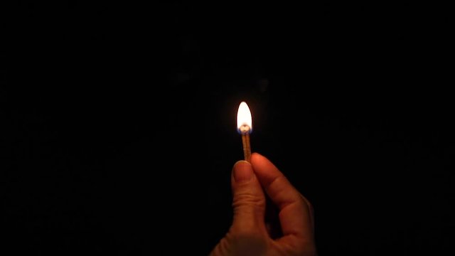 The hand holding matchstick has been ignited in the dark.
