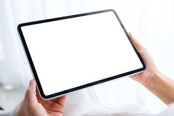 Mockup image of a woman holding black tablet pc with blank white desktop screen while sitting in...