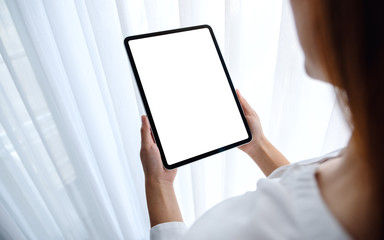 Mockup image of a woman holding black tablet pc with blank white desktop screen in bedroom with feeling relaxed
