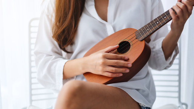 Closeup image of a woman sitting and playing ukulele in bedroom