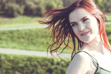 Beautiful girl with red hair in the wind. A woman is looking back with a smile. Psychological concept. Copy space