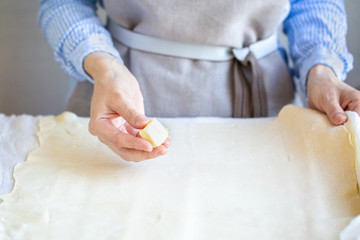 Butter the dough. Cooking apple strudel. Girl is preparing a pie at home in an apron. Work with puff pastry. Hands in oil. The process of making apple strudel
