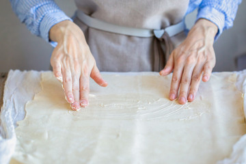 Butter the dough. Cooking apple strudel. Girl is preparing a pie at home in an apron. Work with puff pastry. Hands in oil. The process of making apple strudel
