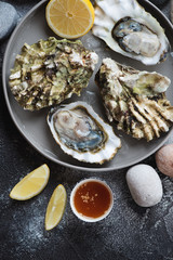 Round grey plate with opened oysters and lemon, above view on a dark grey stone surface, vertical shot, closeup