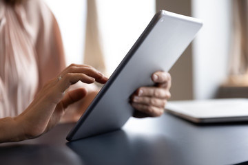 Close up female hands holding computer tablet, using gadget, typing on screen, young woman using electronic device, chatting in social network, writing message, browsing apps, sitting at desk